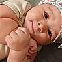 baby, infant, child, face, arm, hand, hat, clothing, smile, cute, skin, lying_down, closeup, expression, chubby, floral_pattern, blanket, soft_texture, indoor, portrait