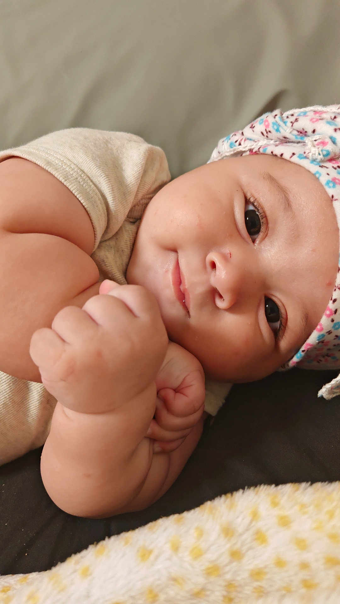 Hichem a rejoint le concours — aidez-le/la à gagner de superbes lots ! baby, infant, child, face, arm, hand, hat, clothing, smile, cute, skin, lying_down, closeup, expression, chubby, floral_pattern, blanket, soft_texture, indoor, portrait