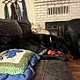 dog, couch, living_room, fireplace, toy, black_dog, light_colored_dog, leather, quilt, coat_rack, wood_floor, indoor, pet, resting, furniture, decor, casual, relaxing, animal, home