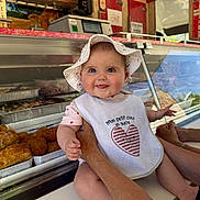 Judith a rejoint le concours — aidez-le/la à gagner de superbes lots ! arm, baby, bib, child, clothing, counter, cute, deli, face, food_display, glass_case, hands, happy, hat, indoor, infant, market, pastries, person, smile