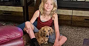 Romeo is registered to the contest to win money with this photo: blonde_hair, boots, carpet, casual_clothing, child, companion, couch, decor, dog, furniture, indoor, leather_chair, living_room, pet, relaxing, shelf, sitting, smiling, television, wooden_table