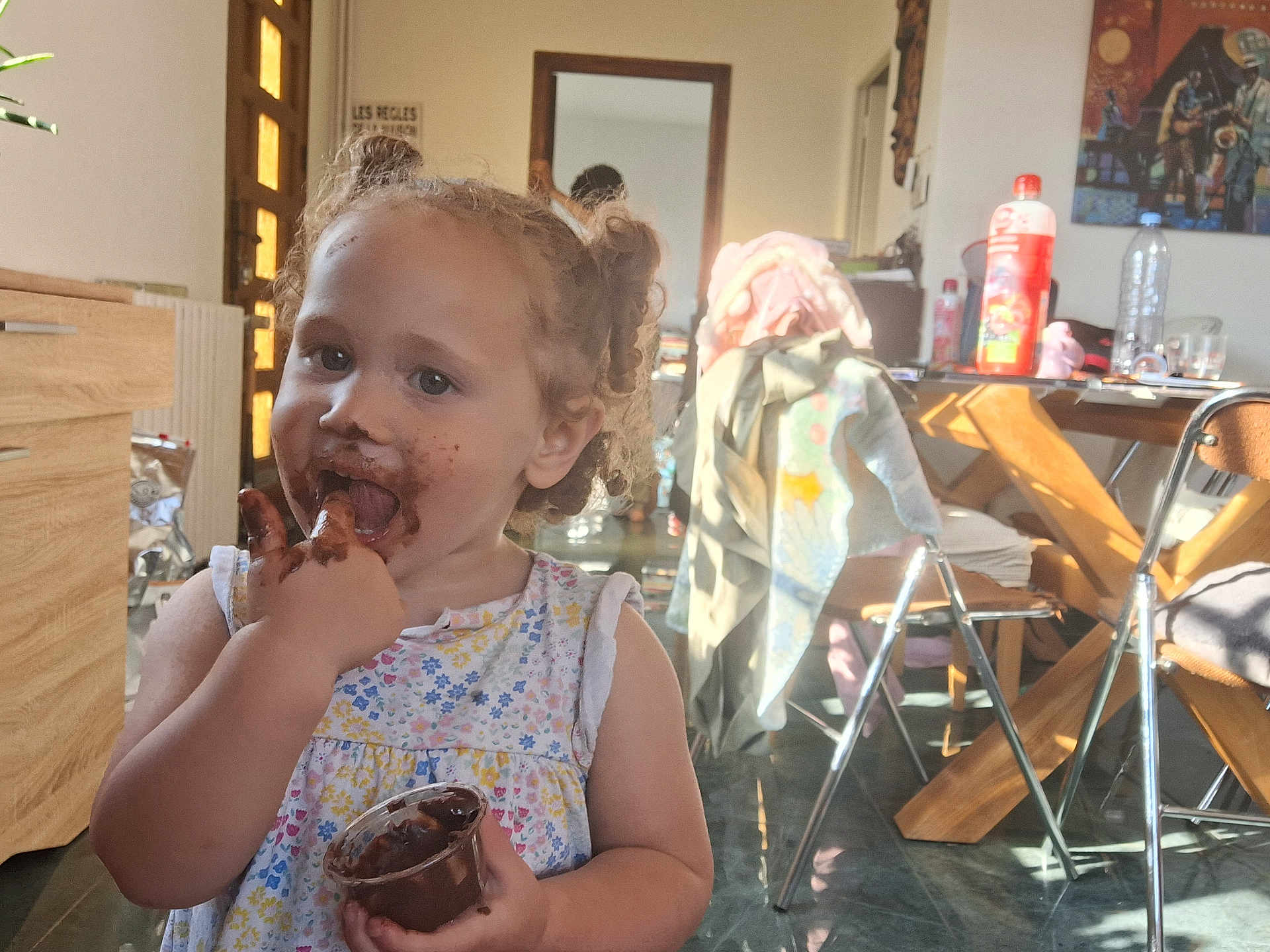 Lounah a rejoint le concours — aidez-le/la à gagner de superbes lots ! toddler, child, chocolate, messy, face, fingers, indoor, kitchen, table, chair, clothing, bottle, floor, light, window, curly_hair, person, smiling, eating, cup