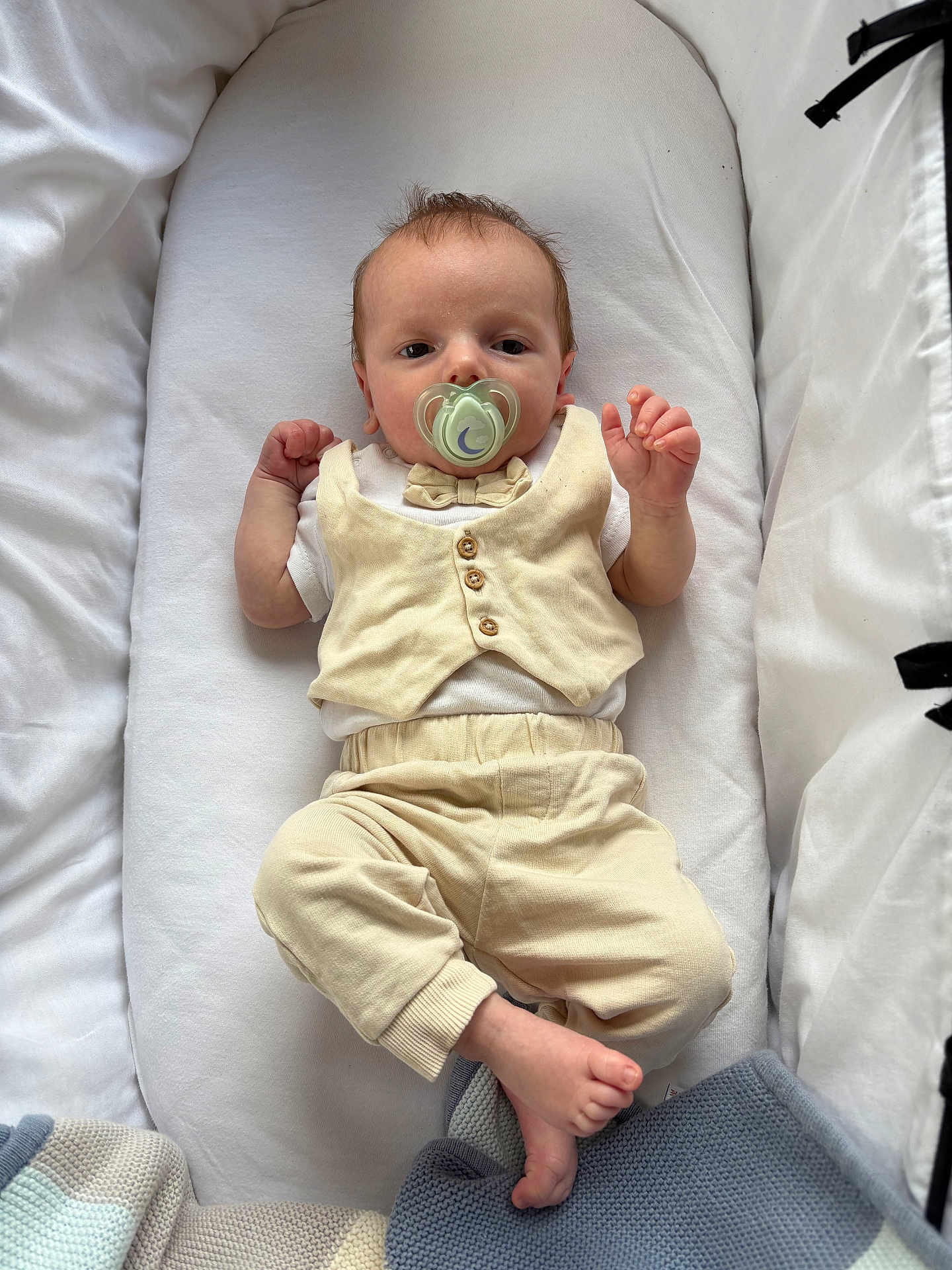 George is registered to the contest to win money with this photo: baby, infant, pacifier, vest, pants, blanket, lying_down, indoors, soft_texture, white_background, foot, hand, cute, child, newborn, sleeping_area, comfort, portrait, peaceful, cozy