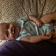 Maddie is registered to the contest to win money with this photo: baby, infant, smiling, onesie, heart_pattern, blanket, lying_down, arm, hand, face, head, soft_lighting, indoor, cozy, cute, person, child, skin, expression, comfort