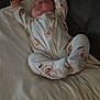 baby, sleeping, pajamas, floral_pattern, pillow, blanket, couch, infant, cozy, indoors, resting, child, soft_lighting, peaceful, hands_up, footed_pajamas, person, relaxation, home, cute