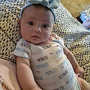 Maddie is registered to the contest to win money with this photo: arm, baby, bow, closeup, curious, cute, face, floor, hand, headband, indoors, infant, lying_down, onesie, patterned_blanket, person, princess, soft_lighting, stone_floor, young_child
