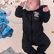 Marceau a rejoint le concours — aidez-le/la à gagner de superbes lots ! baby, sleeping, pacifier, black_onesie, nike_logo, blanket, plush_toy, stitch_toy, gray_knitted_item, infant, cute, indoors, soft_texture, child, resting, small_hands, black_socks, portrait, adorable, young