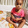 toddler, baby, child, crib, blanket, snack, container, pink_shirt, hair_beads, pigtails, lion_pattern, bedroom, indoor, sitting, curious, cute, face, hands, feet, expression
