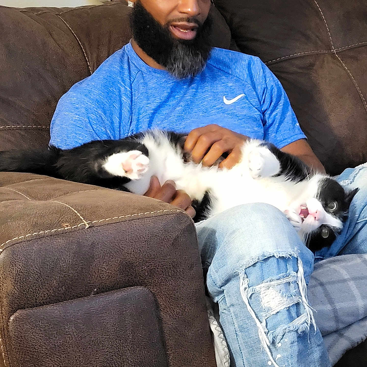 Cosmo is registered to the contest to win money with this photo: beard, black_and_white_cat, blue_shirt, brown_couch, casual, cat, comfort, couch, cozy, furniture, home, indoor, lap, man, petting, playful, relaxed, ripped_jeans, seated, smiling