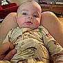 Tommy joined the competition — help win amazing prizes! baby, infant, pajamas, fish_pattern, person, hand, lap, living_room, couch, furniture, television, wooden_cabinet, carpet, indoor, face, child, cozy, curious, seated, casual