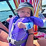 baby, life_jacket, hat, boat, water, towel, person, sunlight, outdoor, summer, child, holding, smile, clothing, blue_sky, nature, recreation, vacation, fun, family