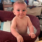 Jdee is registered to the contest to win money with this photo: baby, child, smiling, face, hands, playpen, cushion, indoor, person, young_child, skin, expression, looking_at_camera, cute, infant, happy, standing, blurry_background, home, furniture
