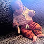 baby, infant, child, knitted_blanket, striped_shirt, pants, barefoot, indoors, soft_lighting, curious_expression, couch, cozy, seated, portrait, warm_colors, young_child, cute, small_hands, small_feet, relaxed