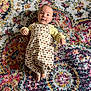 baby, infant, child, romper, patterned_clothing, carpet, colorful, texture, indoor, portrait, smiling, cute, face, hands, feet, lying_down, bright, happy, small, person