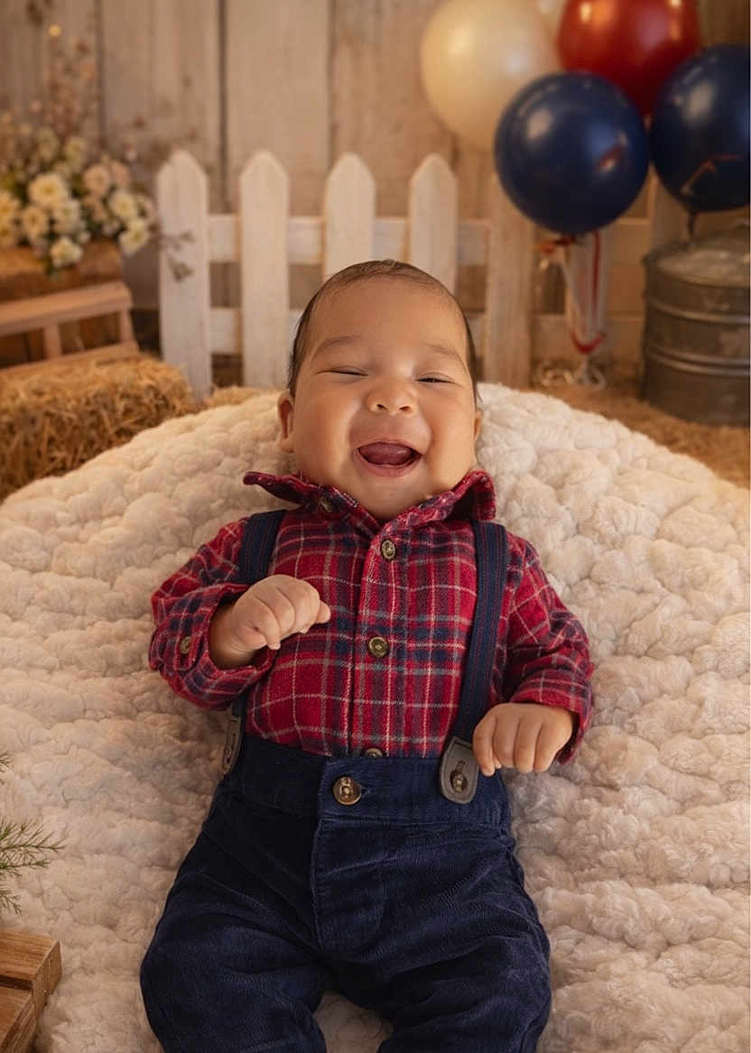 Noah is registered to the contest to win money with this photo: baby, smiling, plaid_shirt, suspenders, navy_pants, blanket, balloons, wooden_fence, hay_bale, rustic, happy, infant, cozy, festive, indoor, cute, portrait, child, soft_texture, celebration