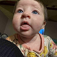 Raelynn is registered to the contest to win money with this photo: baby, child, blue_eyes, tongue, onesie, floral_pattern, indoor, closeup, curious, face, skin, person, infant, cute, young, expression, head, mouth, clothing, portrait