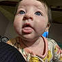 baby, child, blue_eyes, tongue, onesie, floral_pattern, indoor, closeup, curious, face, skin, person, infant, cute, young, expression, head, mouth, clothing, portrait