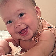 Ariah is registered to the contest to win money with this photo: baby, smiling, happy, infant, closeup, face, skin, arm, earring, pacifier, bracelet, clothing, cute, child, portrait, lying_down, indoors, soft_lighting, baby_girl, expression
