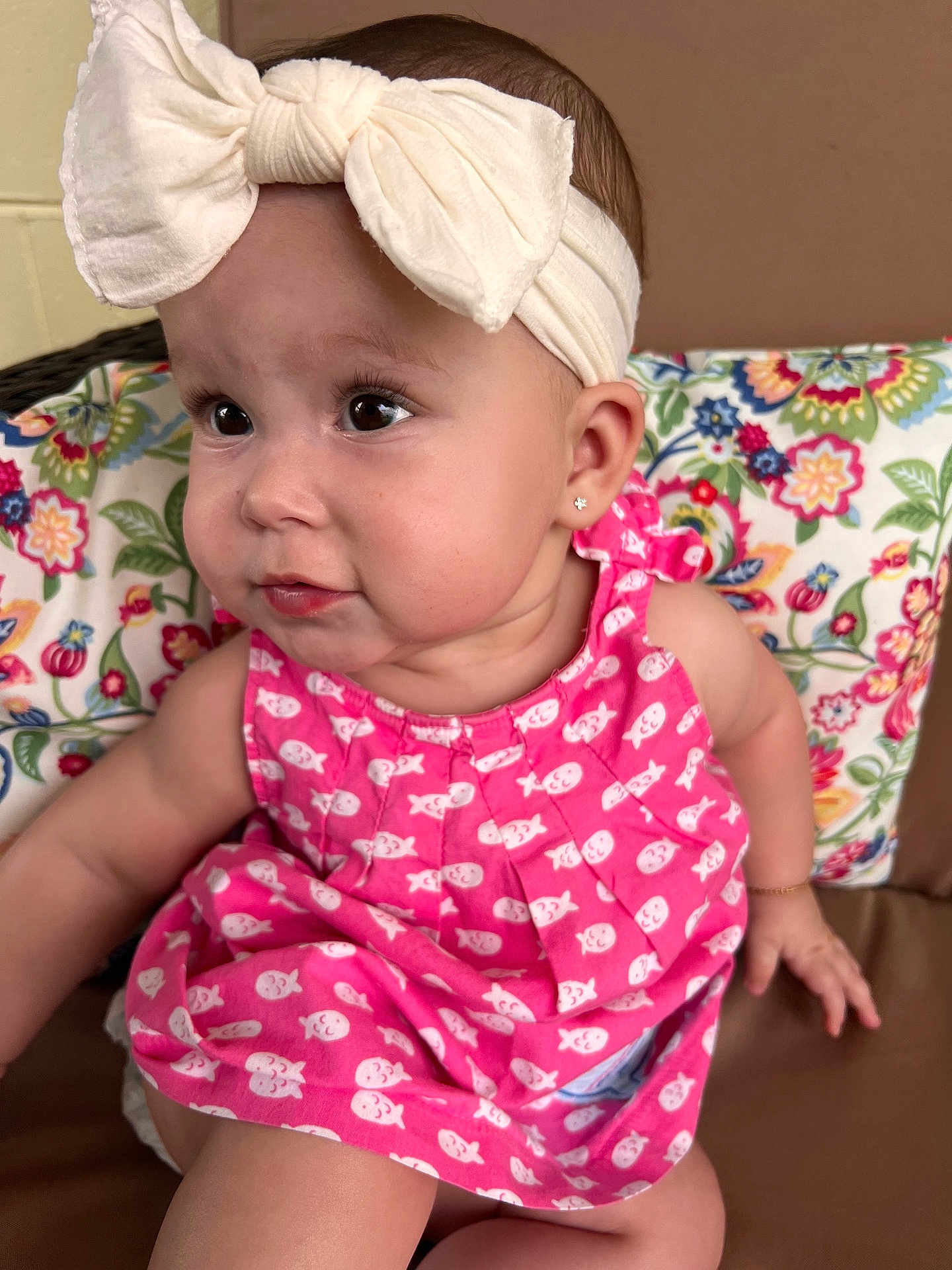 Ariah is registered to the contest to win money with this photo: baby, child, headband, bow, pink_dress, fish_pattern, earrings, cushion, floral_pattern, indoor, cute, sitting, portrait, face, skin, person, young_child, expression, clothing, head