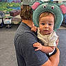Madelynn is registered to the contest to win money with this photo: toddler, child, baby, inflatable_hat, elephant_hat, person, adult, holding, indoor, mural, shopping_cart, gray_shirt, cap, curious, expression, casual_clothing, hand, portrait, background, store