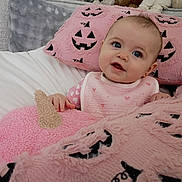 Vanna is registered to the contest to win money with this photo: baby, infant, child, portrait, smiling, blue_eyes, bed, blanket, pink, pumpkin, halloween, plush, cozy, indoors, sitting, bib, clothing, couch, soft_texture, cute