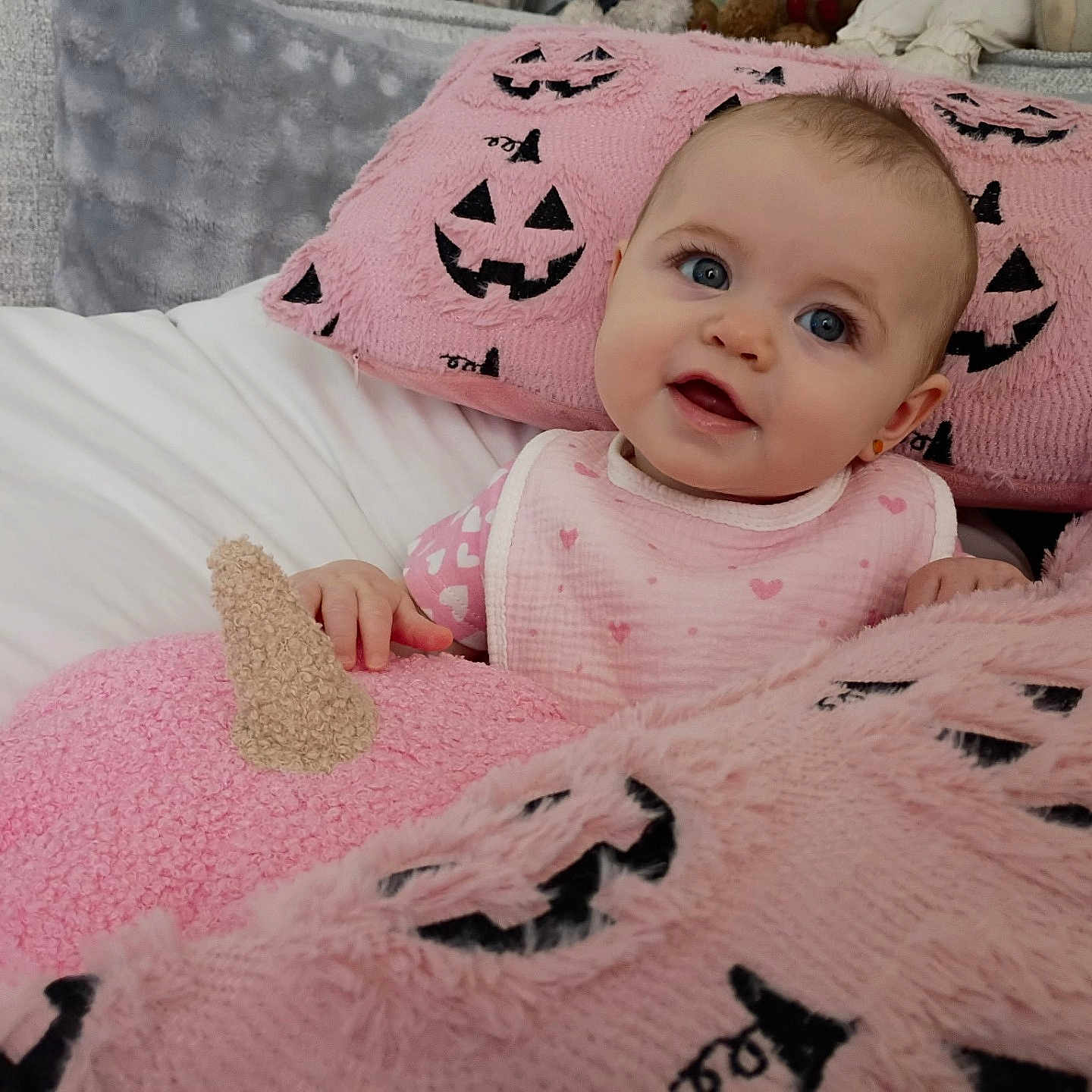 Vanna is registered to the contest to win money with this photo: baby, infant, child, portrait, smiling, blue_eyes, bed, blanket, pink, pumpkin, halloween, plush, cozy, indoors, sitting, bib, clothing, couch, soft_texture, cute