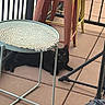 animal, balcony, black_cat, cat, feline, furniture, green_eyes, long_hair, lying_down, metal_railing, outdoor, patio, pet, placemat, portrait, resting, stool, stroller, table, tiled_floor