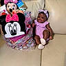 baby, infant, plush_toy, minnie_mouse, gift_basket, couch, leather, headband, purple_clothing, smiling, sitting, child, toy, indoor, cute, comfortable, decorative_wrap, soft_toys, happy, home
