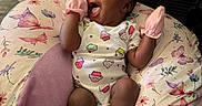 Zahara is registered to the contest to win money with this photo: baby, infant, mittens, socks, pillow, butterfly_pattern, floral_pattern, smiling, happy, cute, indoors, couch, cushion, clothing, person, newborn, portrait, resting, pink, cozy