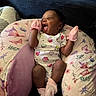 baby, infant, mittens, socks, pillow, butterfly_pattern, floral_pattern, smiling, happy, cute, indoors, couch, cushion, clothing, person, newborn, portrait, resting, pink, cozy