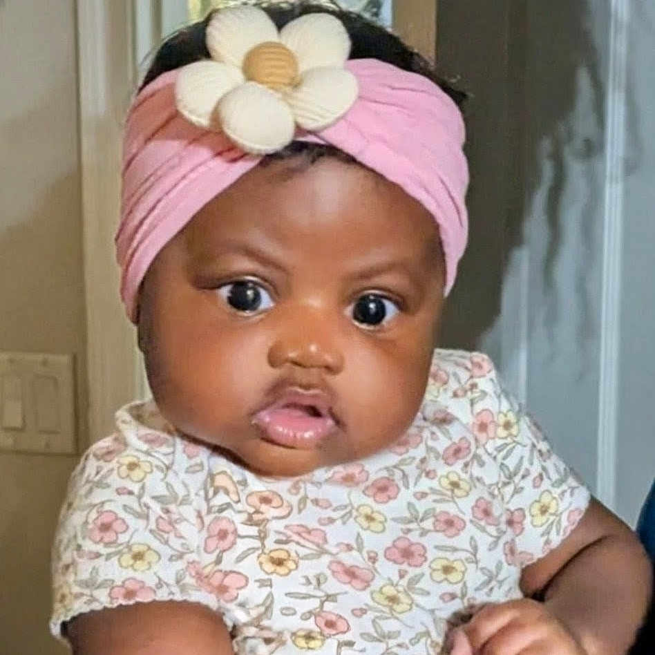 Zahara is registered to the contest to win money with this photo: baby, infant, pink_headband, flower_accessory, floral_outfit, chubby_cheeks, wide_eyes, indoor, portrait, cute, child, headwear, expression, skin, person, young_child, adorable, closeup, baby_girl, fashion
