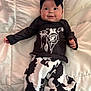 baby, infant, smile, black_bow, headband, cow_print, pants, shirt, lying_down, white_quilt, clothing, cute, child, portrait, indoors, happy, person, fashion, baby_fashion, soft