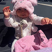 Soulana Espinoza is registered to the contest to win money with this photo: baby, blanket, car, child, clothing, cute, daytime, fluffy_hat, headwear, infant, outdoor, parking_lot, pink_blanket, pink_hat, playful, purple_blanket, reaching_hands, smiling, sunlight, young_child