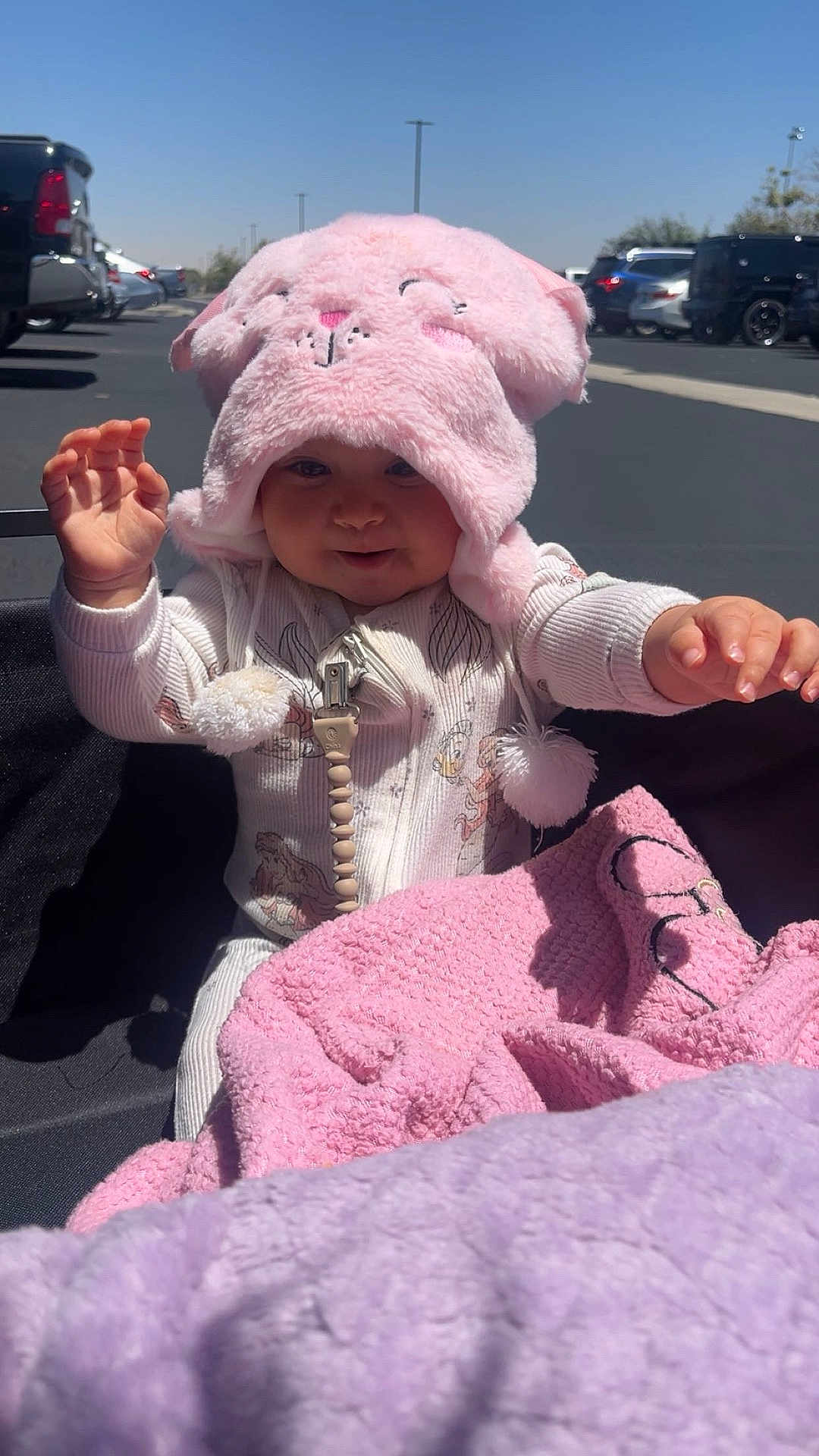 Soulana Espinoza is registered to the contest to win money with this photo: baby, blanket, car, child, clothing, cute, daytime, fluffy_hat, headwear, infant, outdoor, parking_lot, pink_blanket, pink_hat, playful, purple_blanket, reaching_hands, smiling, sunlight, young_child