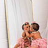 Delilah is registered to the contest to win money with this photo: baby, child, mirror, reflection, pink_tutu, pearls, headband, flower_crown, cute, adorable, indoor, floor, wall, decor, portrait, sitting, playful, self_love, curiosity, skin