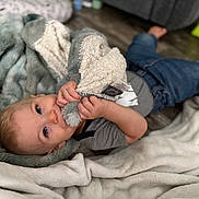 Silas joined the competition — help win amazing prizes! baby, blanket, blue_eyes, casual_clothing, child, comfort, cozy, cute, floor, gray_shirt, hands, home, indoor, infant, jeans, lying_down, plush_toy, relaxing, soft_texture, young