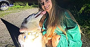 Arayah is registered to the contest to win money with this photo: woman, dog, smiling, night, outdoor, green_dress, pet, happy, grass, gravel, car, collar, long_hair, shadow, face, licking, crouching, nature, friendship, light