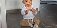 Malo participe au concours pour gagner de l'argent avec cette photo : baby, child, smiling, clapping, sitting, floor, tile, indoor, white_shirt, beige_pants, sock, nursery, crib, toy, room, happy, person, head, face, home