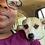 person, dog, glasses, car_interior, window, seat, shoulder, purple_shirt, closeup, pet, companion, affection, calm, indoor, resting, brown_eyes, light, seatbelt, casual, friendship