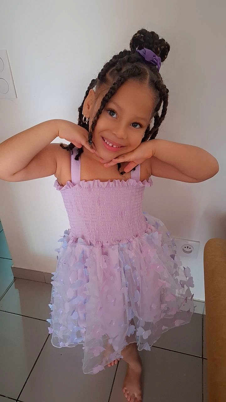 Lyana participe au concours pour gagner de l'argent avec cette photo : child, girl, smiling, braided_hair, hair_bun, purple_dress, tulle_skirt, flower_appliques, pose, hands_under_chin, barefoot, indoor, tiled_floor, happy, earrings, big_eyes, portrait, pastel_colors, wall_outlet, playful