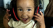 Aaliyah joined the competition — help win amazing prizes! child, toddler, portrait, smiling, happy, headphones, gaming_headset, curly_hair, indoor, living_room, seated, shirt, denim, skirt, hands, camera, close_up, joyful, home, music