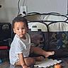Aaliyah is registered to the contest to win money with this photo: toddler, child, sitting, indoors, playroom, playpen, toy, puzzle_mat, floor, portrait, face, looking_at_camera, curly_hair, earring, white_shirt, barefoot, sibling, furniture, wall_outlet, home