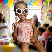 Aaliyah is registered to the contest to win money with this photo: child, toddler, birthday, party, smiling, sunglasses, pink_dress, baby, balloons, birthday_cake, celebration, indoor, seated, portrait, colorful, guests, decorations, happy, one_year_old, ai_generated_content