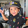 Aaliyah joined the competition — help win amazing prizes! child, toddler, portrait, smiling, happy, indoors, baseball_cap, sports_cap, lakers, basketball, black_shirt, patterned_clothing, pineapple, colorful, raised_hand, sitting, home, blurred_background, closeup, person