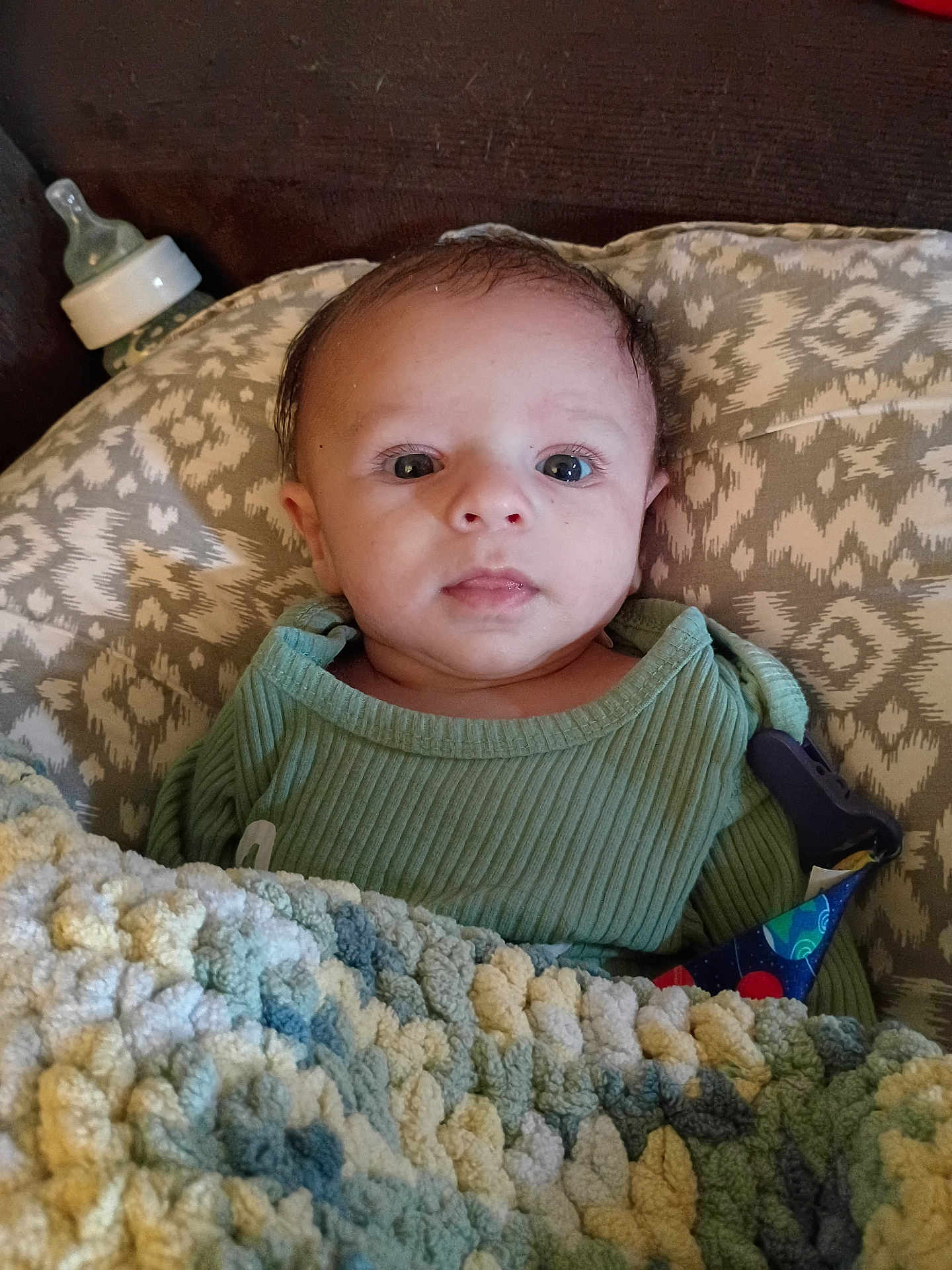 Clifford is registered to the contest to win money with this photo: baby, infant, blanket, bottle, pillow, green_clothing, face, eyes, head, person, portrait, indoors, cozy, patterned, knitted_blanket, resting, cute, young_child, newborn, baby_girl_or_boy