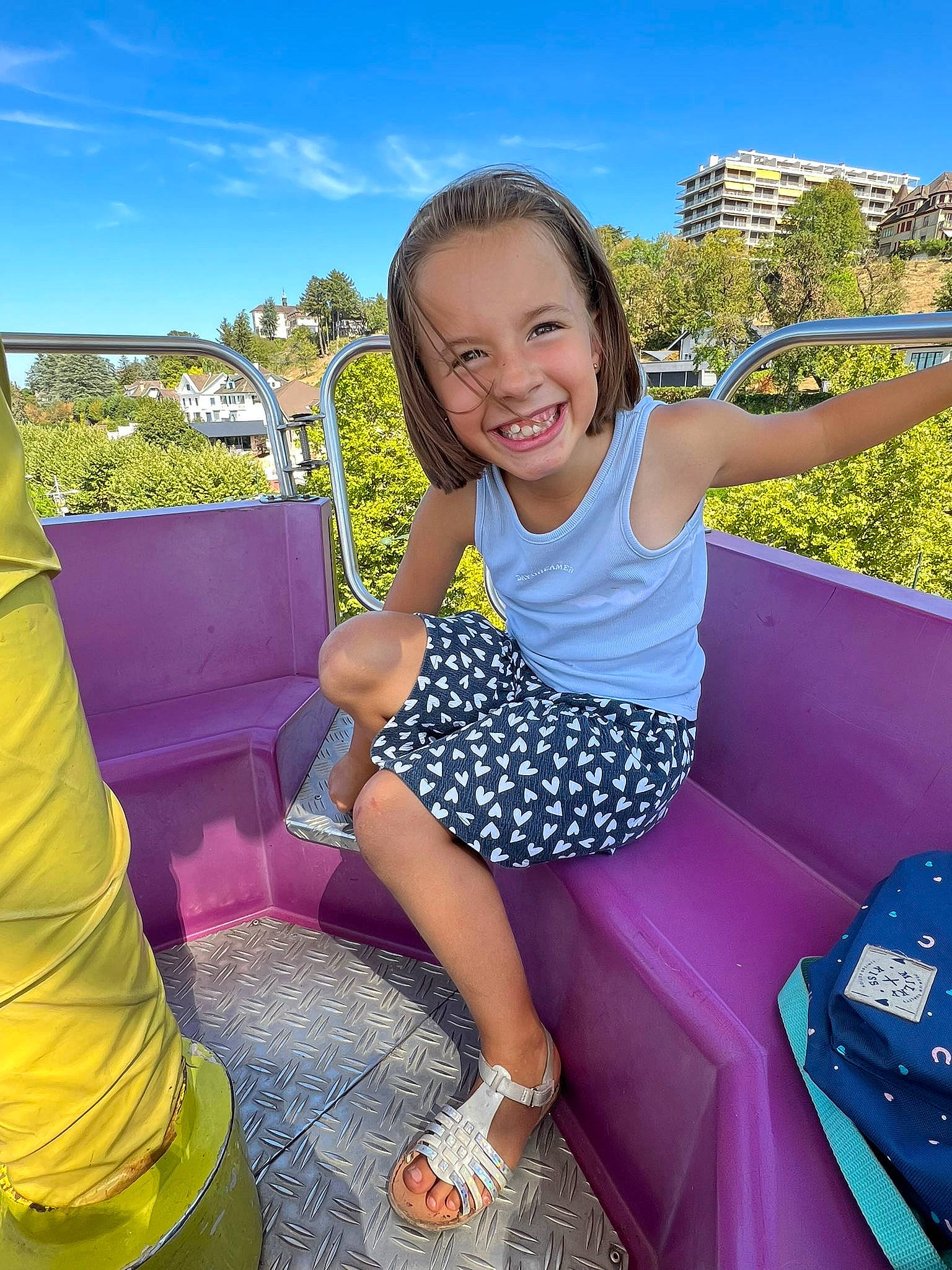 énora a rejoint le concours — aidez-le/la à gagner de superbes lots ! automotive_exterior, blue, bumper, cool, facial_expression, fun, grass, happy, joy, leisure, motor_vehicle, outdoor_play_equipment, person, pink, recreation, sitting, sky, smile, toddler, travel