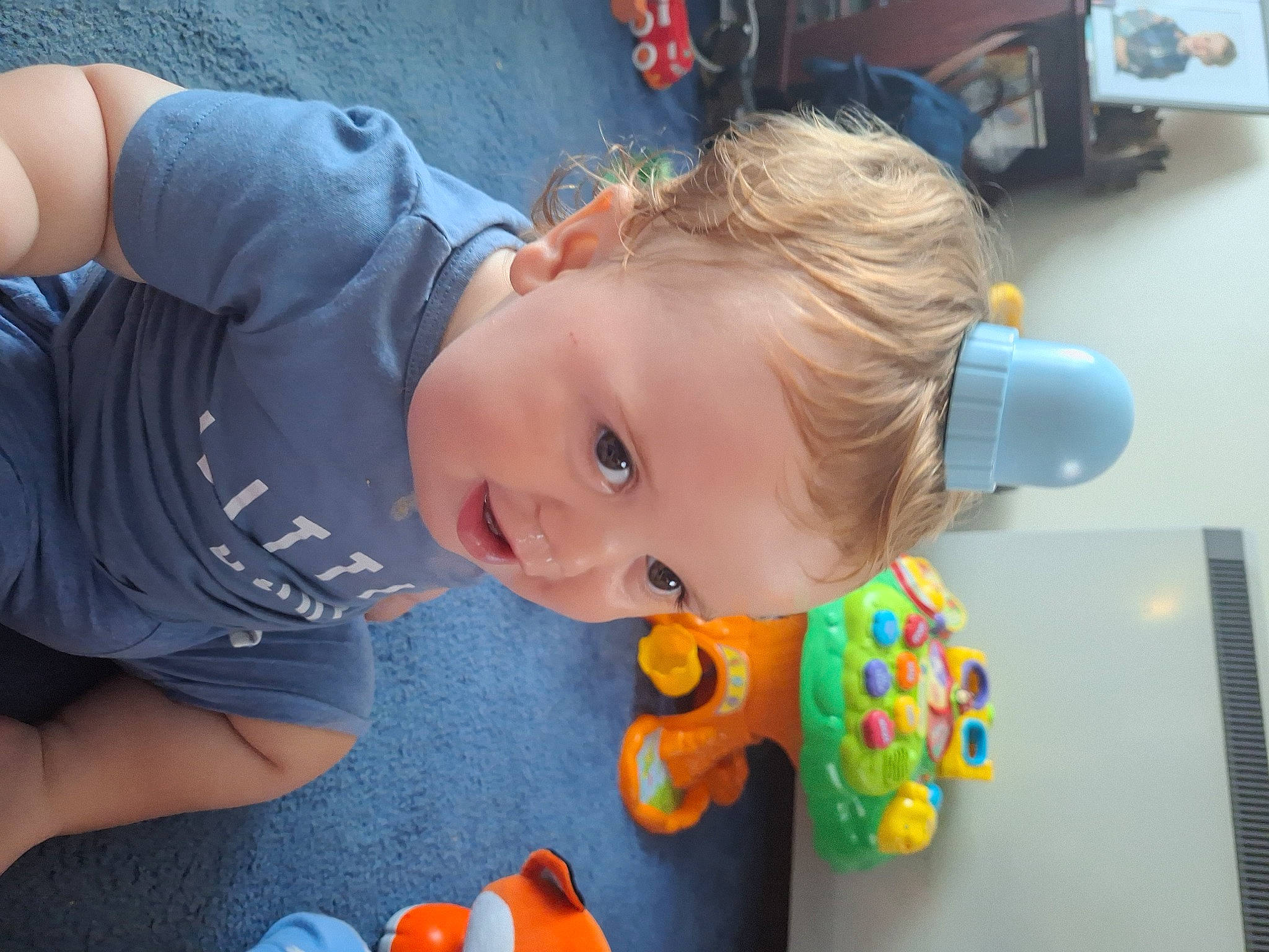 Harrison is registered to the contest to win money with this photo: baby, baby_playing_with_toys, baby_products, baby_toddler_clothing, baby_toys, blue, child, flooring, fun, grass, happy, human_body, leisure, orange, person, play, room, sitting, snapshot, toddler