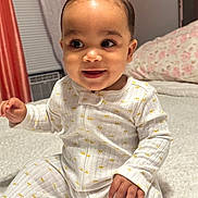 Jaylen Aviles is registered to the contest to win money with this photo: baby, child, pajamas, smile, indoor, bedroom, blanket, soft, curly_hair, cute, infant, happy, sitting, face, person, cozy, young, portrait, home, sleepwear