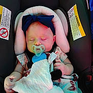 Macie is registered to the contest to win money with this photo: baby, sleeping, pacifier, car_seat, blanket, headband, infant, child, cute, resting, safety, warning_label, clothing, soft, peaceful, indoors, person, small_hand, comfort, adorable