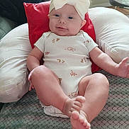 Macie is registered to the contest to win money with this photo: baby, blanket, bow, child, comfortable, couch, cute, feet, headband, home, indoor, infant, legs, living_room, onesie, person, pillow, relaxing, smile, soft